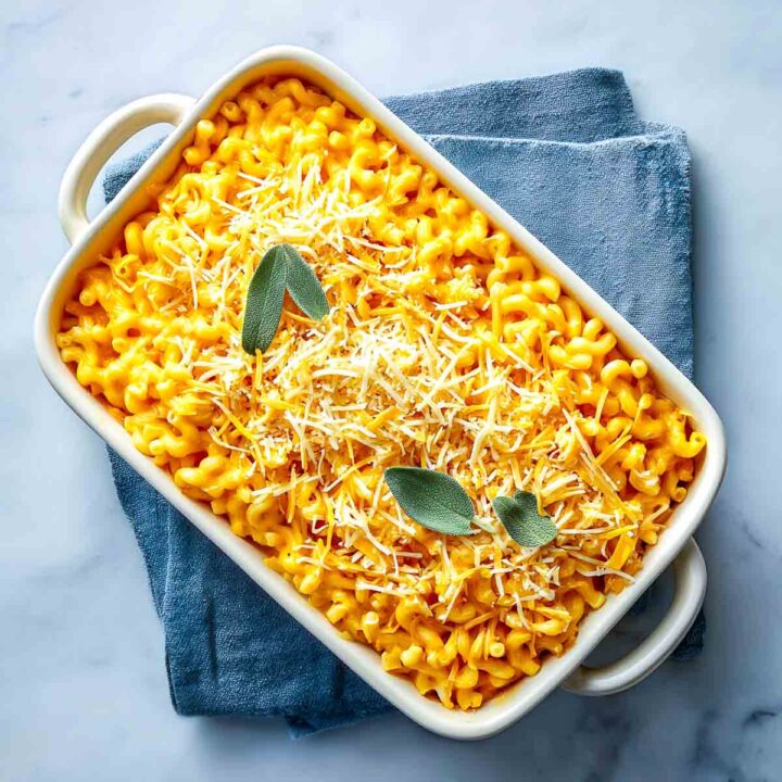 Unbaked pumpkin sage mac and cheese topped with cheese and fresh sage.
