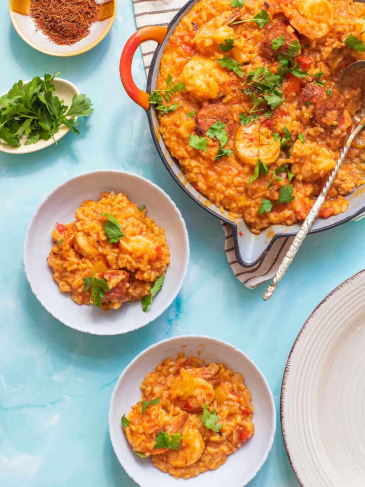 Shrimp saffron paella served in two small white bowls with the paella pan in the background.