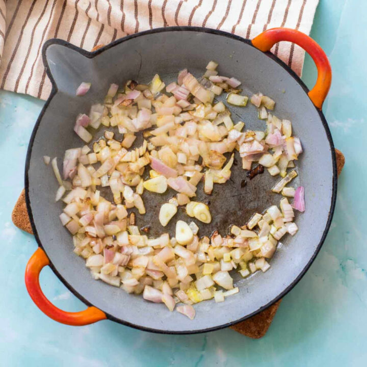 Diced yellow onions and sliced garlic cloves sautéing in a gray paella pan.