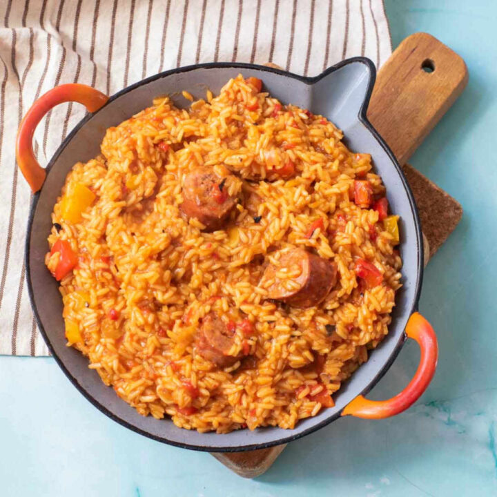 Diced yellow onions and sliced garlic cloves sautéing in a gray paella pan with orange handles.