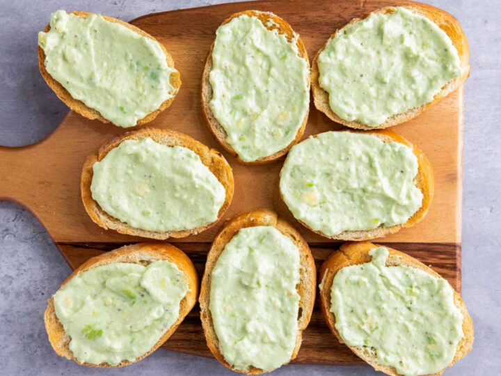 The eight toasted bread slices are arranged on a wooden cutting board, each topped with a generous, even layer of the pale green avocado spread.