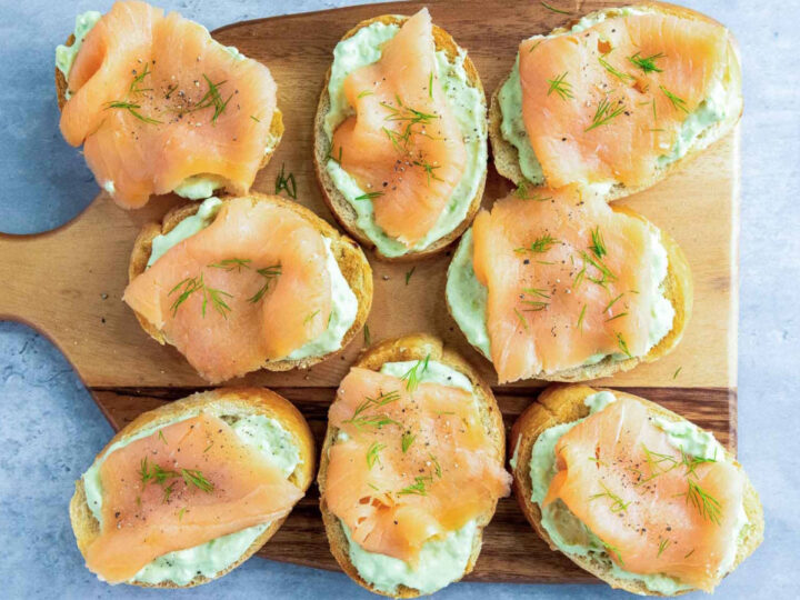 Pieces of smoked salmon are draped over the avocado spread on each slice of toast, then garnished with fresh dill sprigs and cracked black pepper.