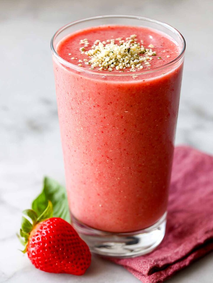 Strawberry basil smoothie in tall glass with hemp hearts on the top.