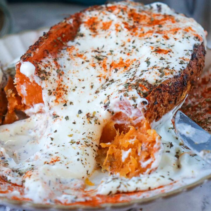 A detailed view of the roasted sweet potato being sliced, showing the soft orange interior mixed with the melting white yogurt and spices.