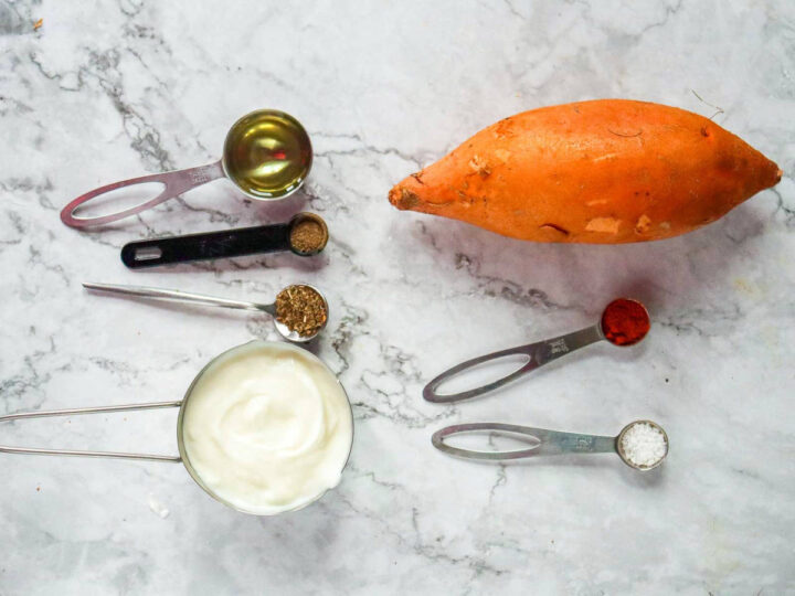 A whole sweet potato, Greek yogurt, oil, and various spices in measuring spoons.