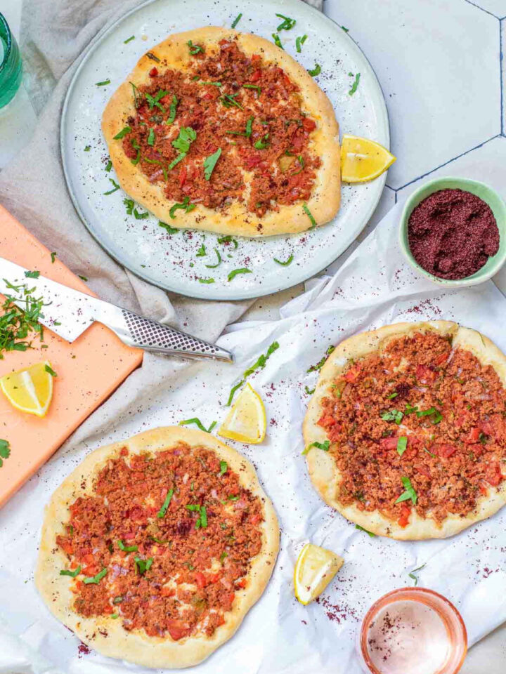 Three Turkish lahmacuns topped with minced meat, herbs, and spices, served with lemon wedges and sumac.