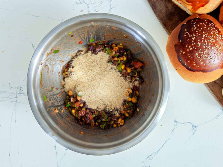 Overhead view of a metal mixing bowl with black bean veggie burger mixture topped with breadcrumbs before mixing.