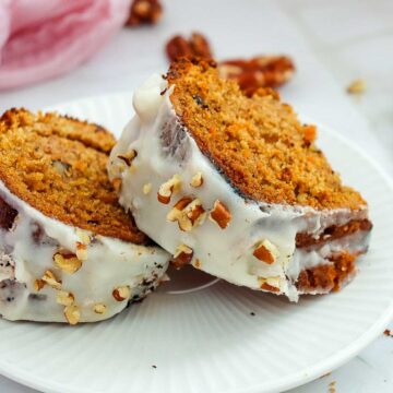 Two thick slices of carrot bundt cake with white cream cheese frosting and chopped pecans on a white plate.