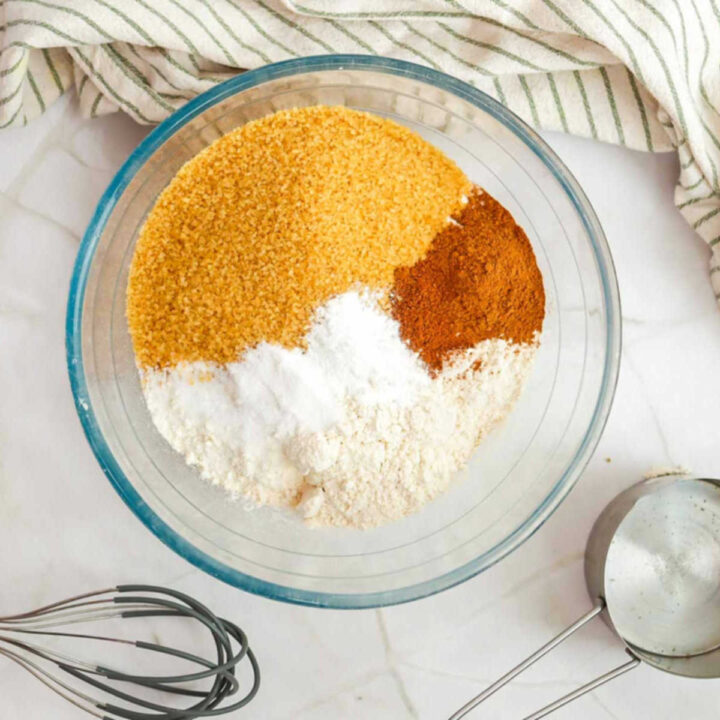 A glass mixing bowl containing flour, brown sugar, baking powder, and cinnamon before being whisked together.