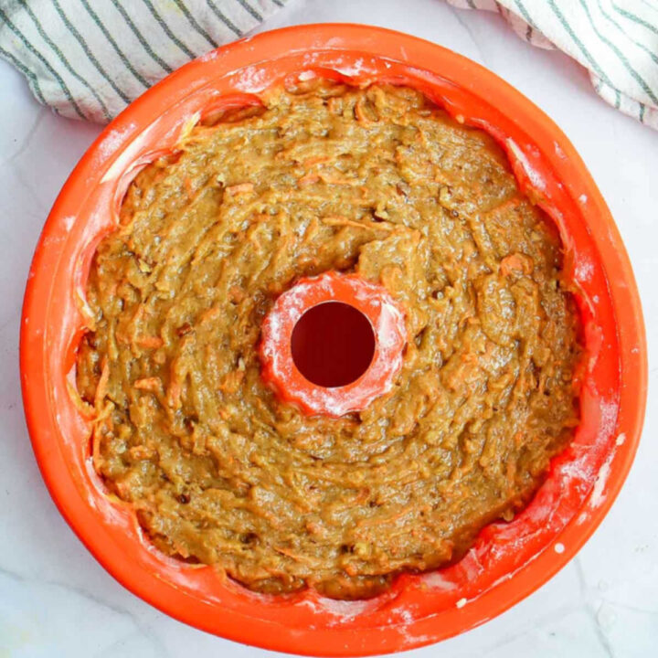 Carrot cake batter smoothed into a greased and floured red silicone bundt pan, ready for baking.