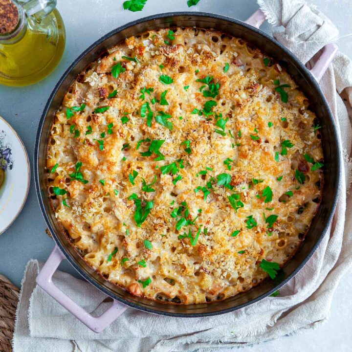 Overhead view of a baked chicken cordon bleu pasta casserole in a round skillet, topped with melted cheese, crispy breadcrumbs, and chopped parsley, with a golden, bubbly surface.