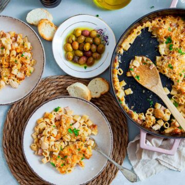 Chicken cordon bleu pasta bake served in two white plates with the skillet in the background.