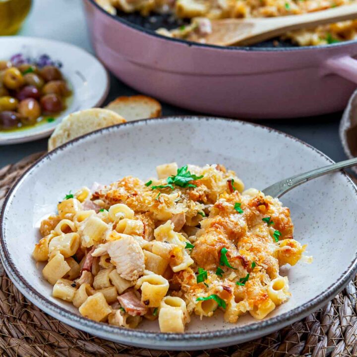 Bowl of chicken cordon bleu pasta bake served with short pasta, tender chicken, ham, and creamy cheese sauce, topped with golden breadcrumbs and fresh parsley, with the baking dish blurred in the background.