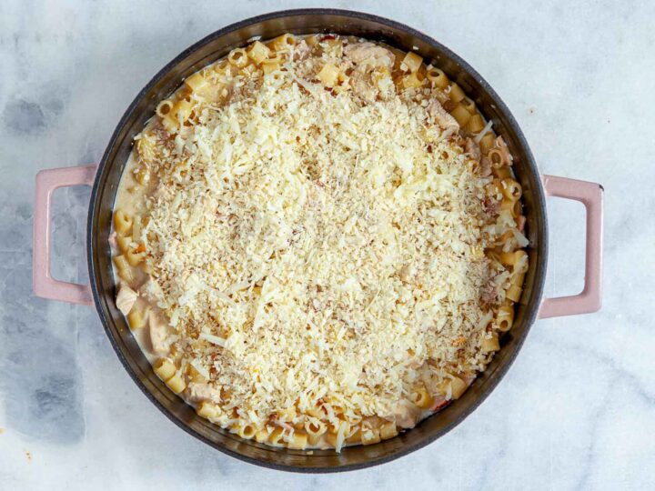 Overhead view of chicken cordon bleu pasta bake in a skillet, fully assembled and topped with a generous layer of shredded cheese and breadcrumbs, ready to be baked.