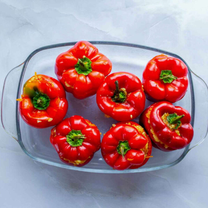 Chicken and rice–stuffed red bell peppers arranged upright in a clear glass baking dish, ready to be baked.