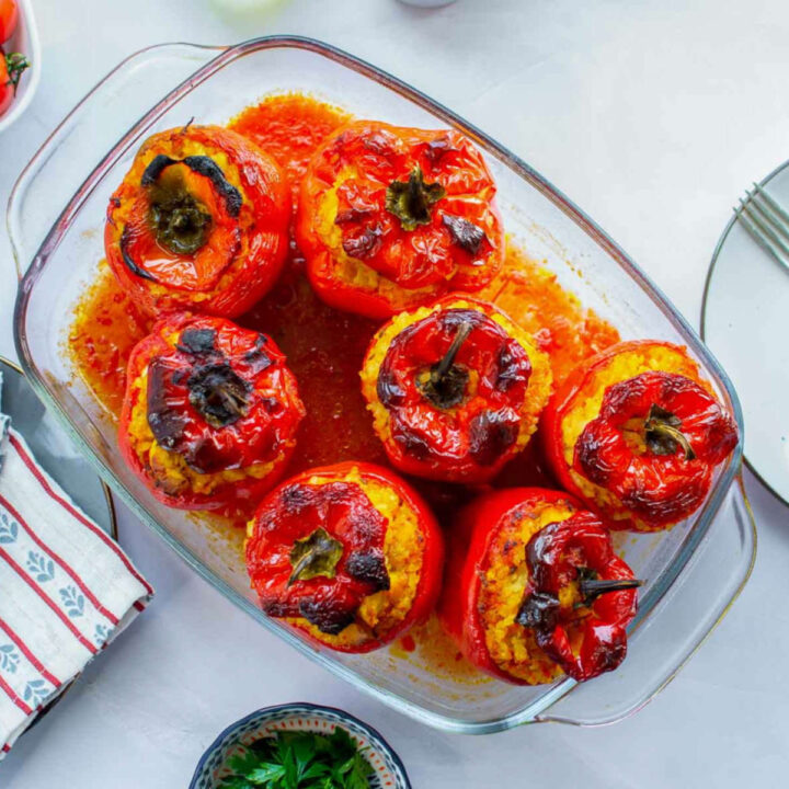 Baked chicken and rice–stuffed red bell peppers with lightly charred tops in a glass baking dish.