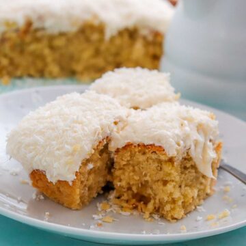 Coconut cake squares with creamy frosting and shredded coconut served on a plate.