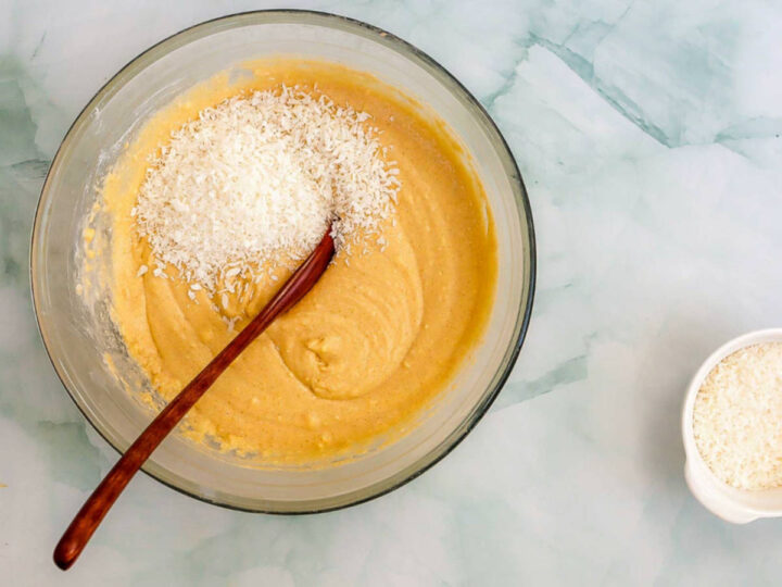 Shredded coconut being folded into coconut cake batter in a mixing bowl.