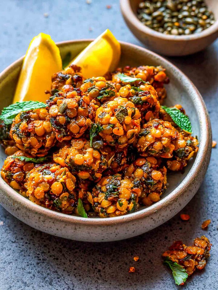 Crispy lentil snack clusters with lemon wedges and fresh herbs served in a grey bowl.