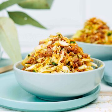 Egg roll bowl made with seasoned ground meat and sautéed cabbage, topped with sesame seeds and served in a light blue bowl.