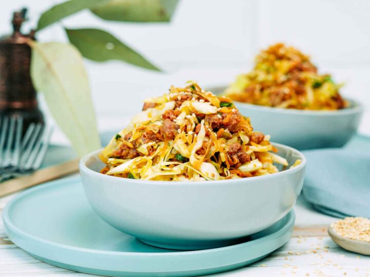 Egg roll bowl made with ground meat, shredded cabbage, and carrots, topped with sesame seeds and served in a light blue bowl.