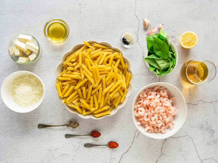 An overhead shot displays the raw ingredients for garlic butter shrimp pasta, including penne, peeled shrimp, fresh basil, garlic, butter, olive oil, parmesan cheese, lemon, white wine, sesame seeds, and various spices. Beside it, the finished dish features the penne and shrimp tossed in a green herb sauce, garnished with shredded cheese, seeds, and lemon wedges.