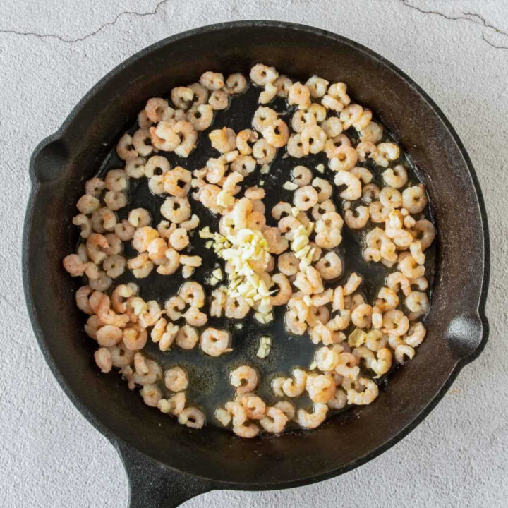 In this step, the small peeled shrimp are sautéed in a cast-iron skillet with minced garlic.