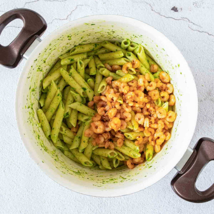 The cooked shrimp are added to the pot of penne pasta, which has been thoroughly coated in the green herb butter.
