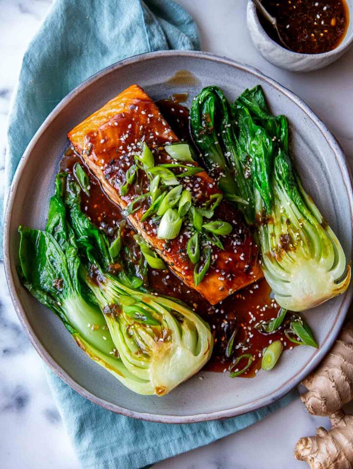 Ginger soy glazed salmon served alongside steamed bok choy on a plate.