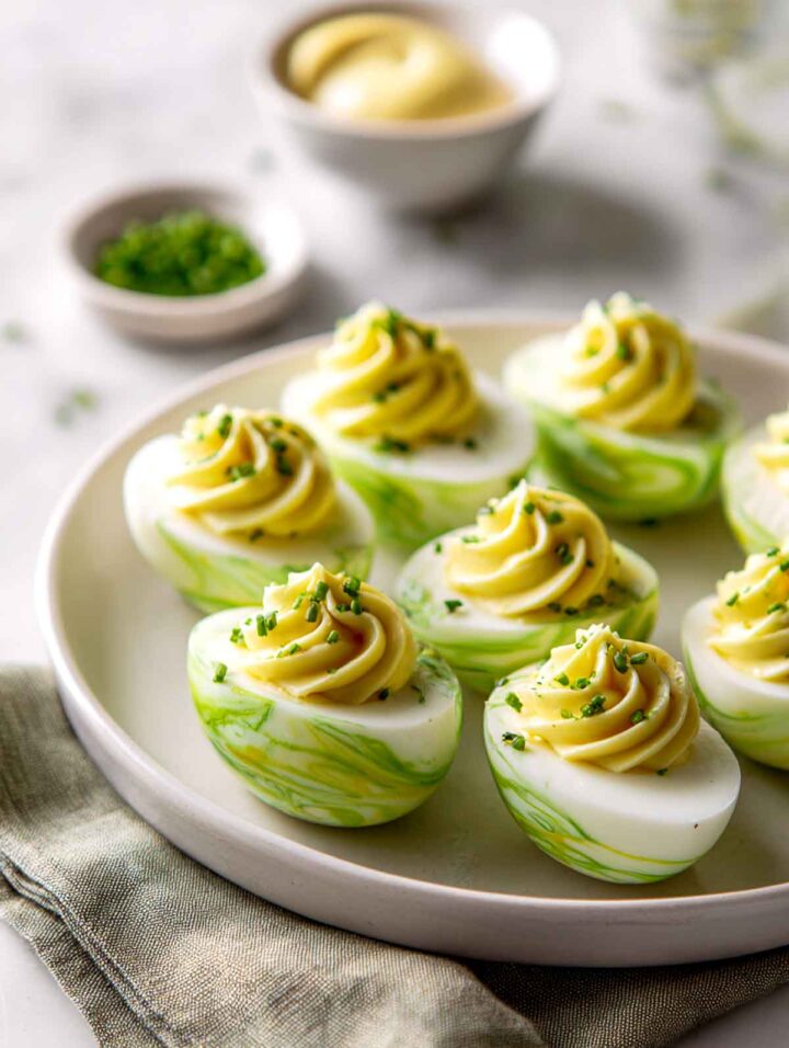 Green marbled deviled eggs with classic filling and chive garnish on marble surface.