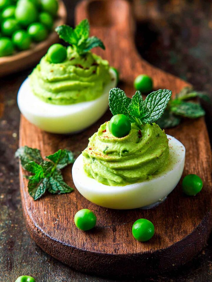 Pea and mint green deviled eggs topped with whole peas and fresh mint leaves.