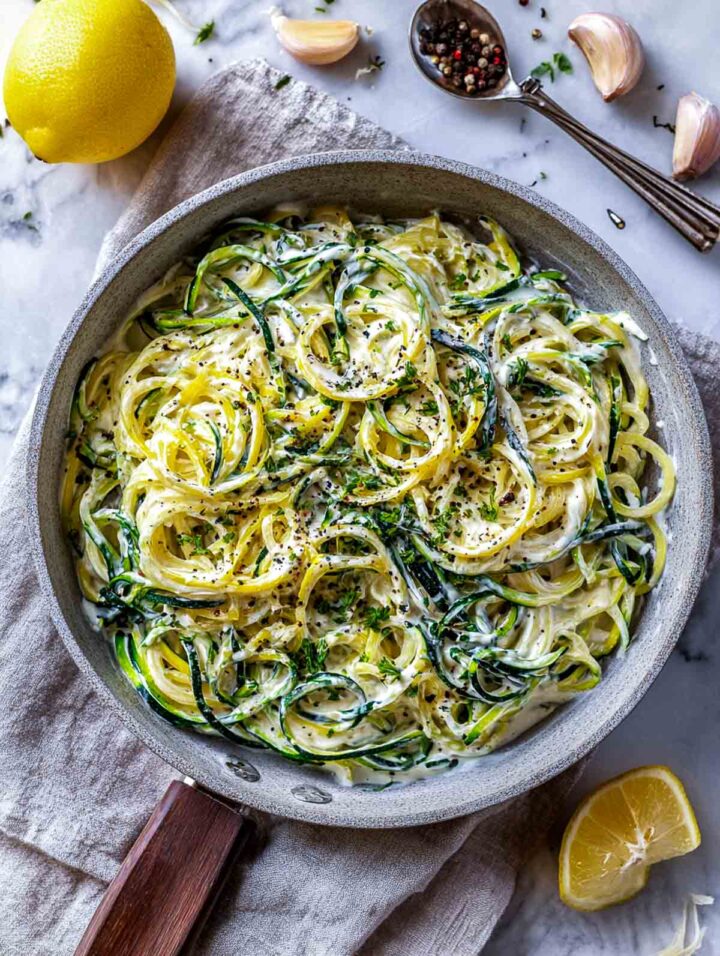 Zucchini noodles tossed with lemon and garlic yogurt sauce in a skillet.