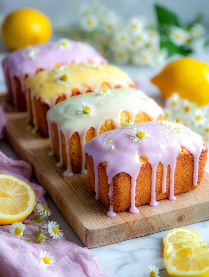 Mini lemon loaf cakes topped with soft pastel glaze on a wooden board.