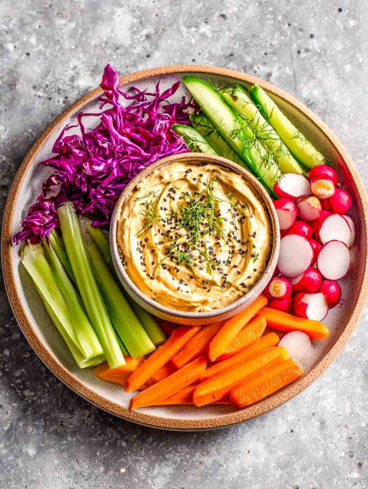 Miso tahini veggie dip with carrots cucumbers and radishes on a brown serving plate.