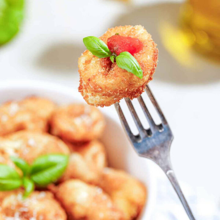 A crispy fried tortellini on a fork with a drop of tomato basil sauce.