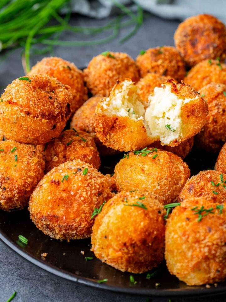 Close up of parmesan herb potato bites with one broken piece to show the cheesy center.
