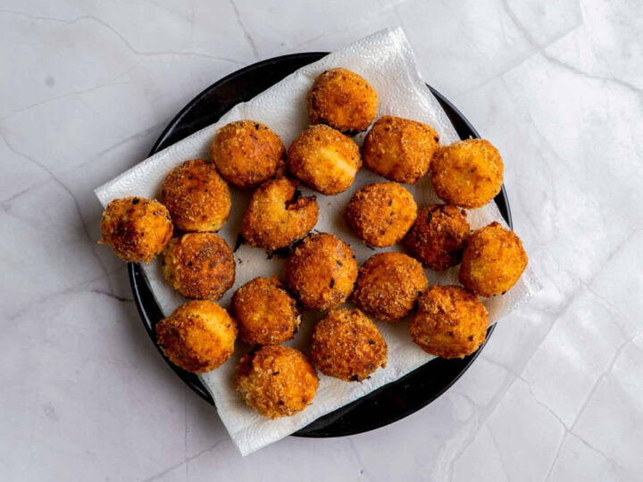 Golden-brown fried potato bites resting on a paper towel–lined black plate, draining excess oil after frying.