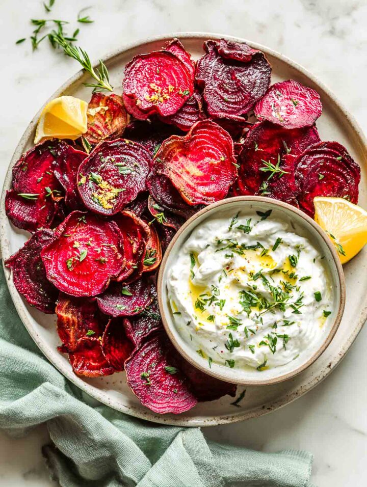 Roasted beet chips served with lemon herb yogurt dip on a white plate.