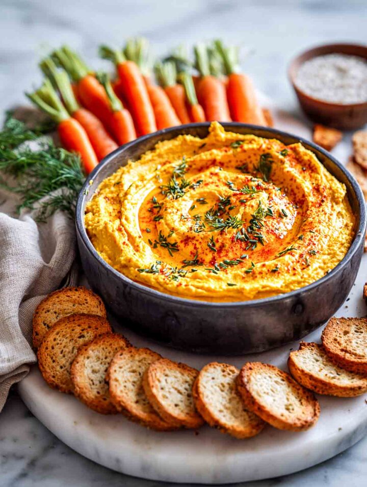 Roasted carrot hummus with fennel seeds served with bread and carrots.