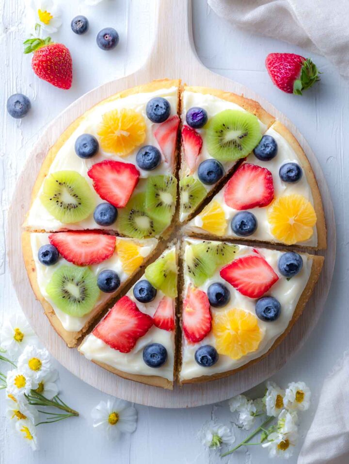 Spring garden fruit pizza cookies sliced into eight wedges with fresh fruit and flowers placed on a wooden pizza board.
