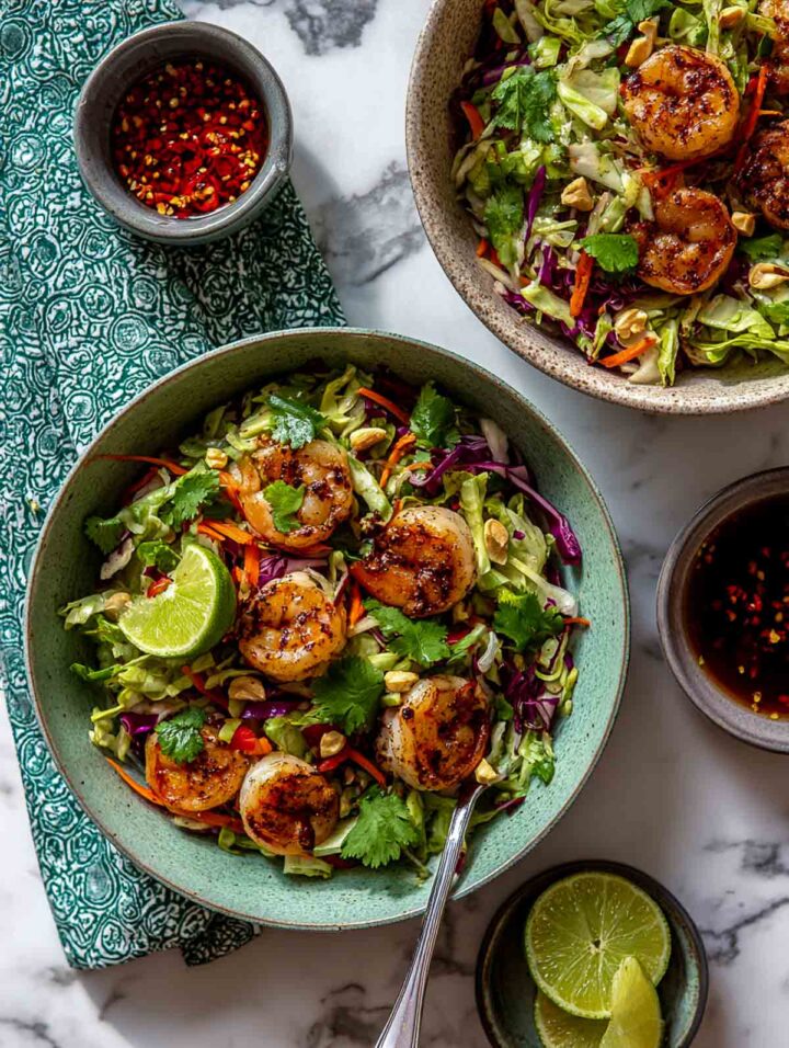 Lime-seasoned shrimp served over shredded cabbage with herbs in a bowl.