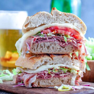 Close-up of a toasted Italian grinder stacked with deli meats, melted cheese, lettuce, and tomato.