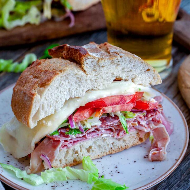 Toasted Italian grinder sandwich with deli meats, melted cheese, lettuce, and tomato served on a plate.