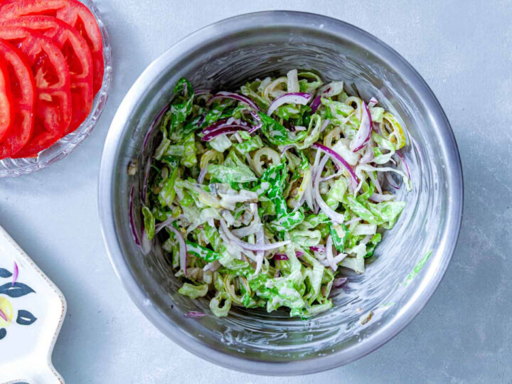 Shredded lettuce and sliced red onion tossed with dressing in a mixing bowl.