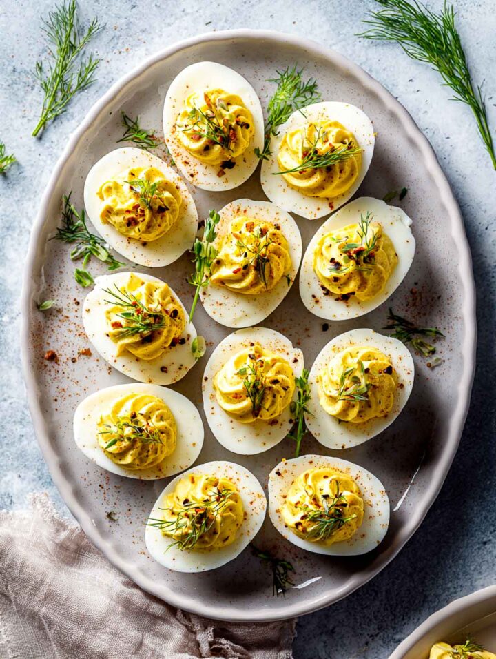 Truffle deviled eggs arranged on a white serving plate garnished with herbs.