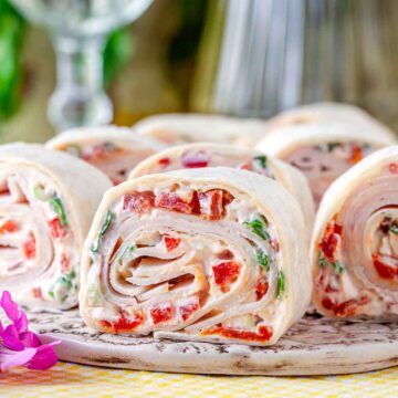 Turkey pinwheel wraps filled with cream cheese, sun-dried tomatoes, and herbs, sliced and served on a platter.