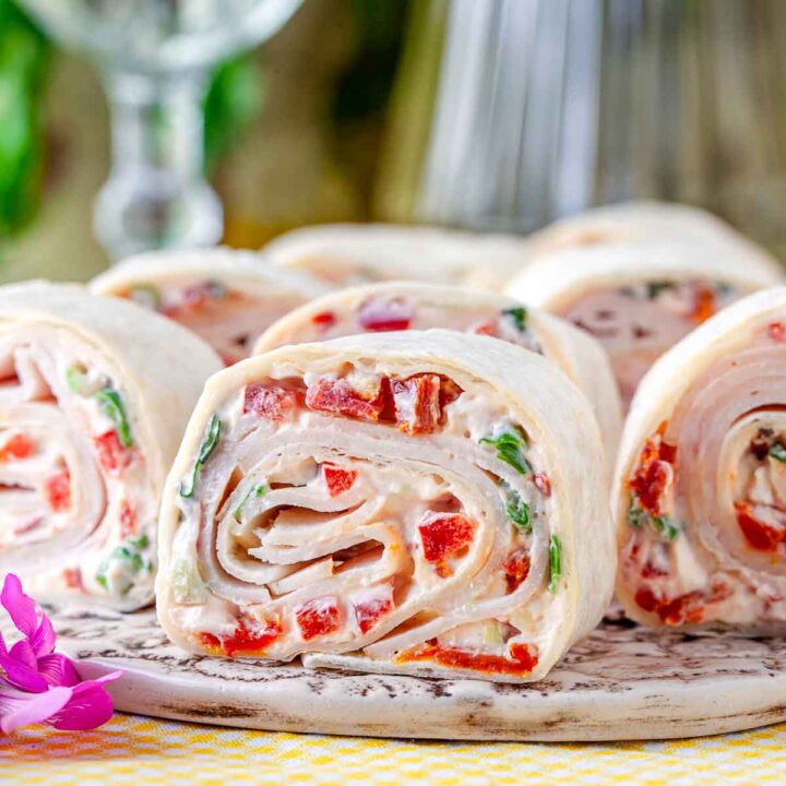 Turkey pinwheel wraps filled with cream cheese, sun-dried tomatoes, and herbs, sliced and served on a platter.