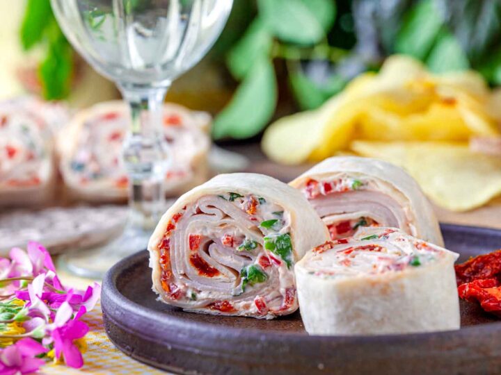 Sliced turkey pinwheels with cream cheese, sun-dried tomatoes, and herbs on a dark serving plate.