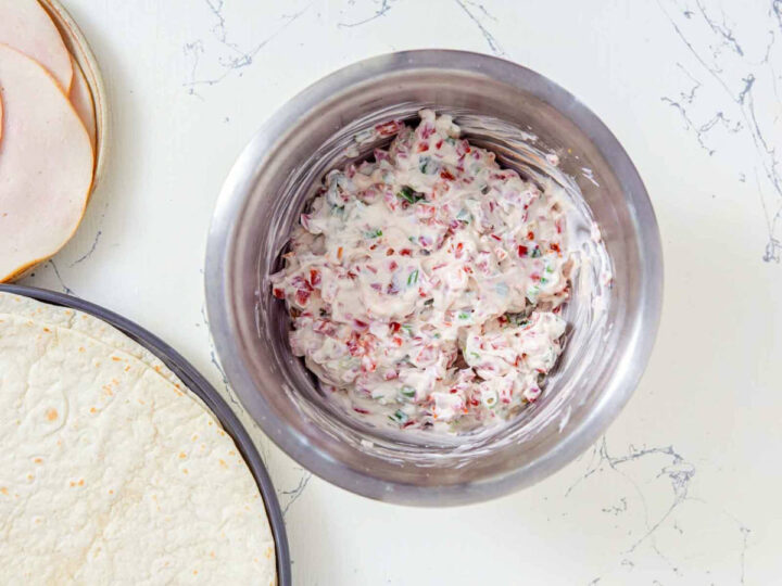 Cream cheese mixture with chopped sun-dried tomatoes and herbs in a mixing bowl.