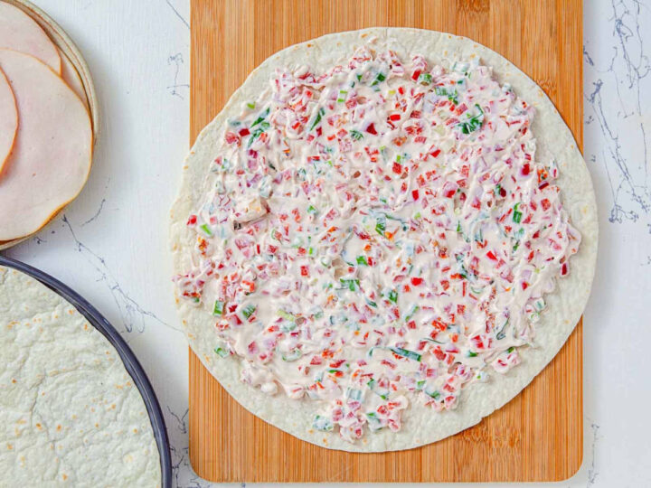 Cream cheese mixture spread evenly over a flour tortilla on a cutting board.